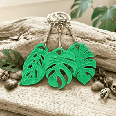 Green leaf-shaped keychains on a wooden surface with natural elements.