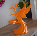 Orange decorative figurine of a fairy with a bird on a wooden surface.