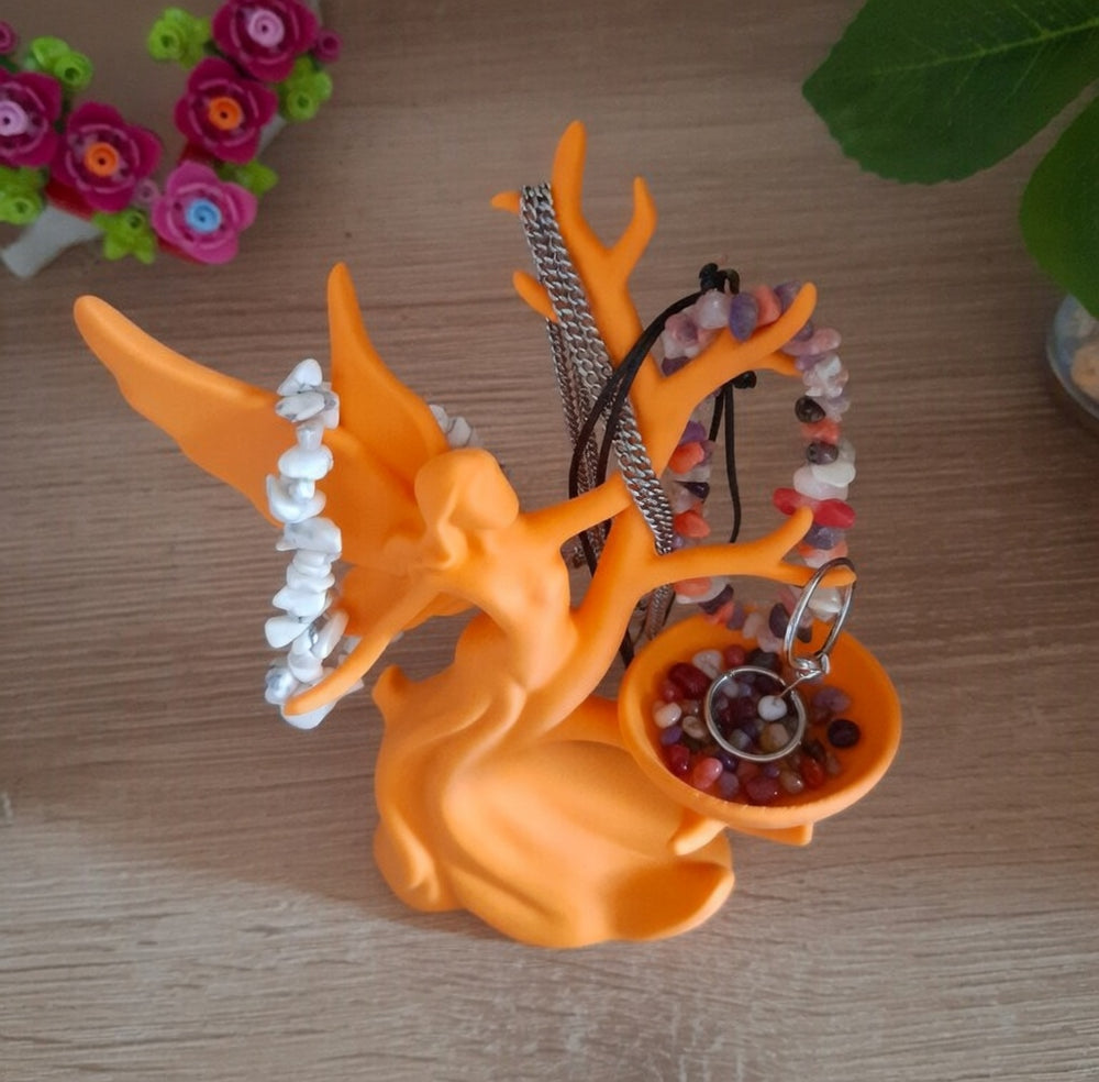 Orange fairy-shaped jewelry holder with necklaces and bracelets on a wooden surface.