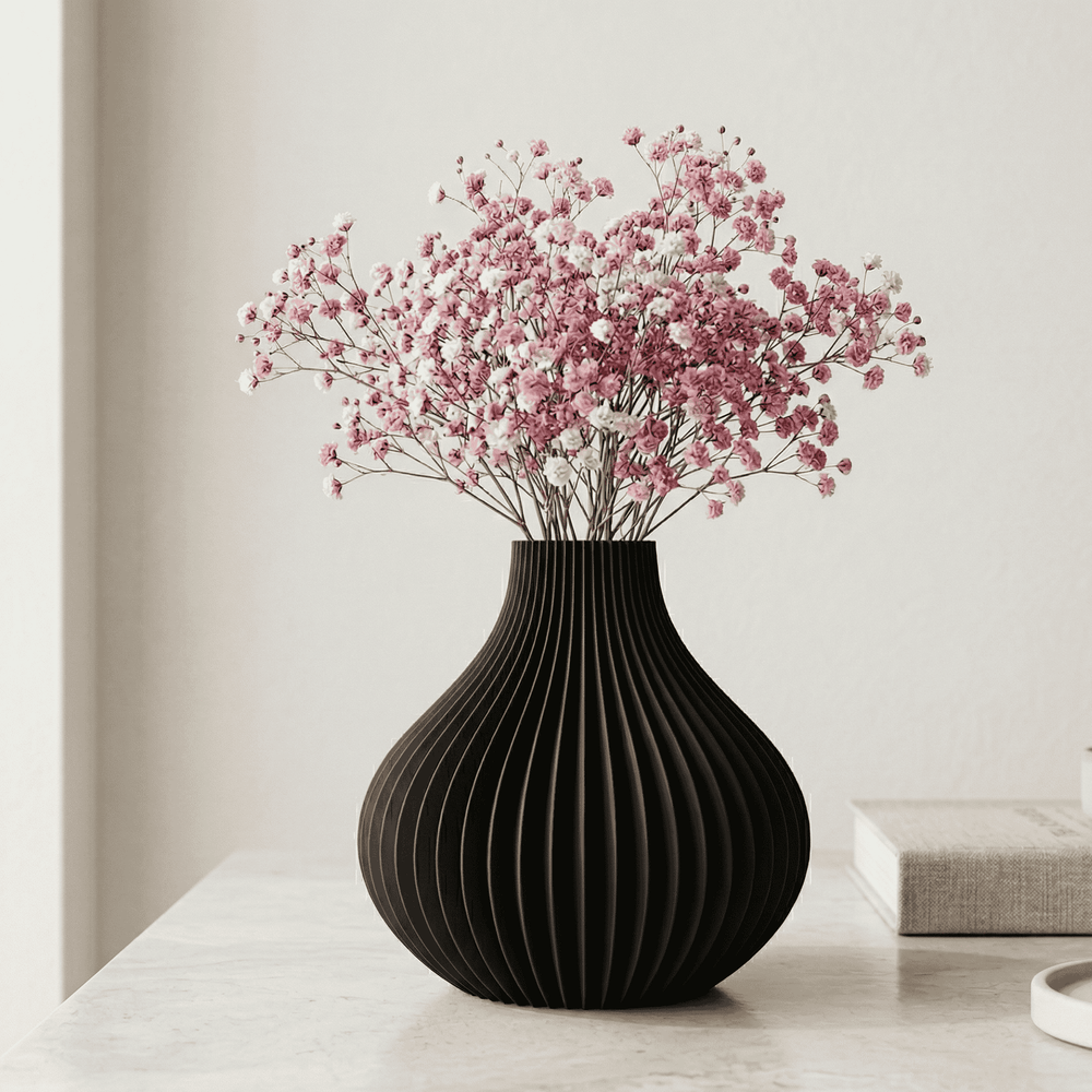 Black vase with pink flowers on a light surface against a neutral background