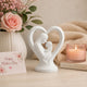 White statue of a mother and child in a heart shape with flowers, card, and candle in the background.