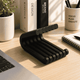 Black pen holder on a desk with books, a plant, and stationery items.
