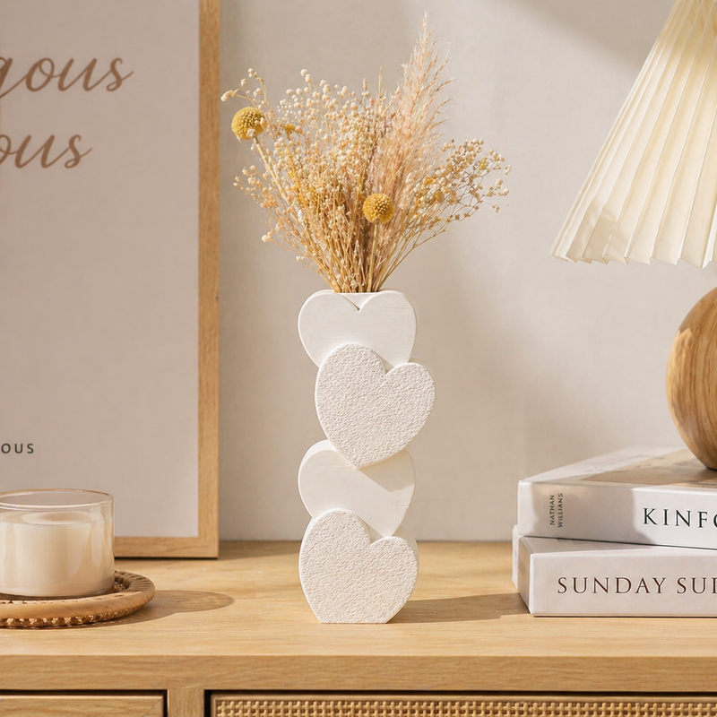 Decorative vase with heart design on a wooden surface with books and a candle.