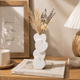 Decorative vase with heart shapes on a wooden surface with a lamp and framed text in the background.